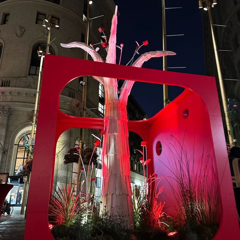 Community Tree at night: the white tree lit pink inside the red cube, small red cubes hanging from its branches.