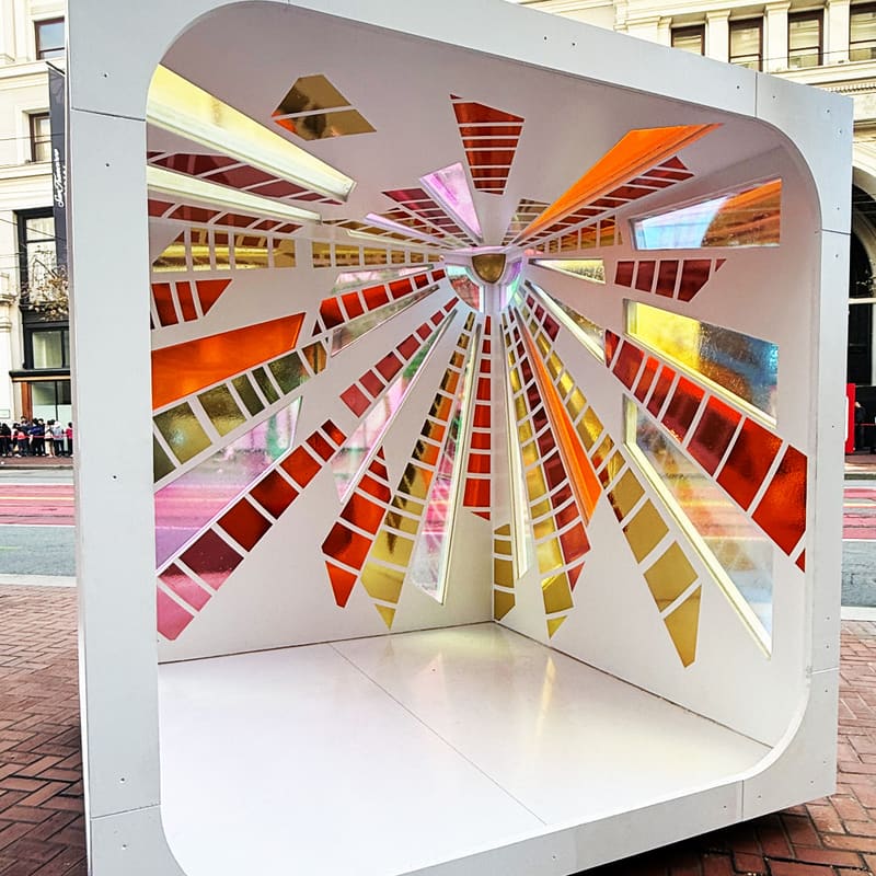 Ray of Light by Raylene Gorum: a white cube with amber, pink and clear glass rays fanning out from a sun at its centre.