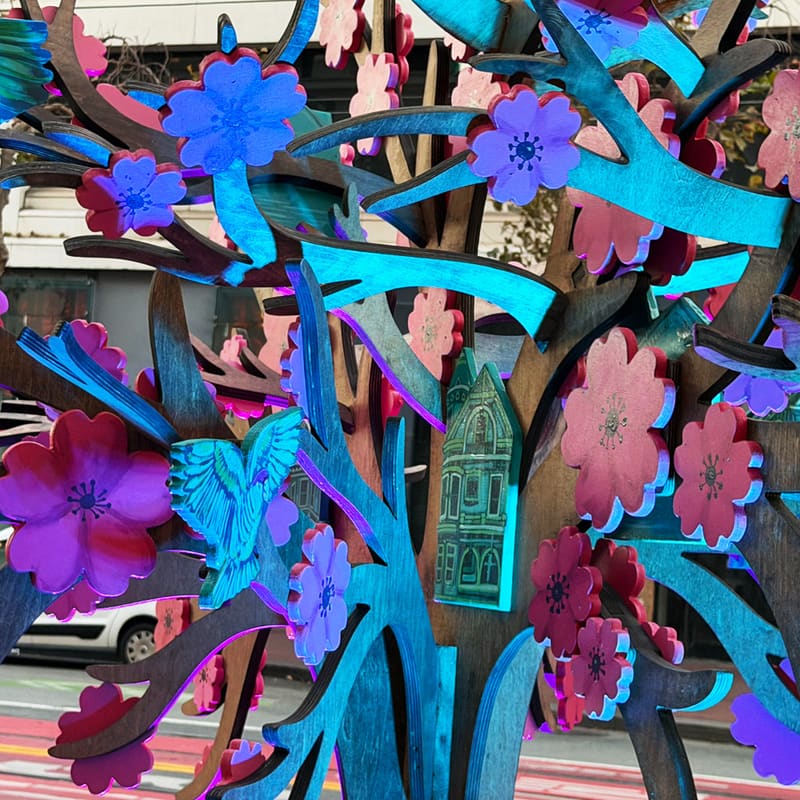 Close-up of Zen Treehouse: pink and purple blossoms, teal branches and birds, and a small teal house hanging among them.